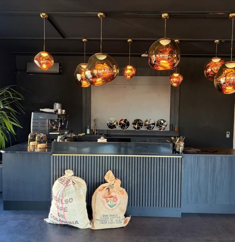 Moderne Espresso-Bar mit schwarzer Theke, goldenen Pendelleuchten und Kaffeesäcken